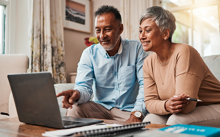 man and woman sitting on couch looking at laptop screen