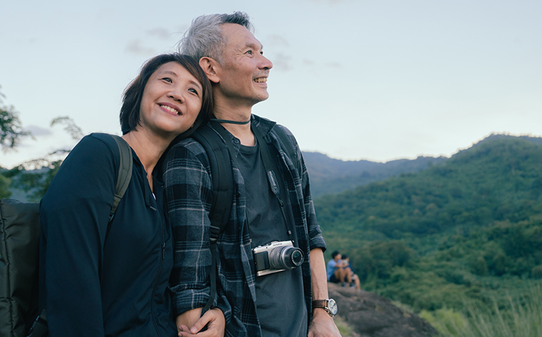 older man and woman smiling outside with mountains in the background